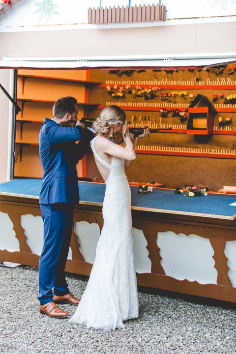 Hochzeitswahn - Braut und Bräutigam stehen an einer Bar und berühren liebevoll ihre Stirnen. Das elegante weiße Kleid der Braut weht hinter ihr her, während der Bräutigam einen eleganten blauen Anzug trägt. Die rustikale Bar-Kulisse ergänzt ihren freudigen Moment.