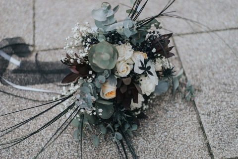 Hochzeitswahn - Ein elegant arrangierter Blumenstrauß mit einer Mischung aus weißen Rosen, Schleierkraut, dunklem Laub und Eukalyptusblättern, der auf einem strukturierten Pflaster ruht und einen sanften Schatten wirft.