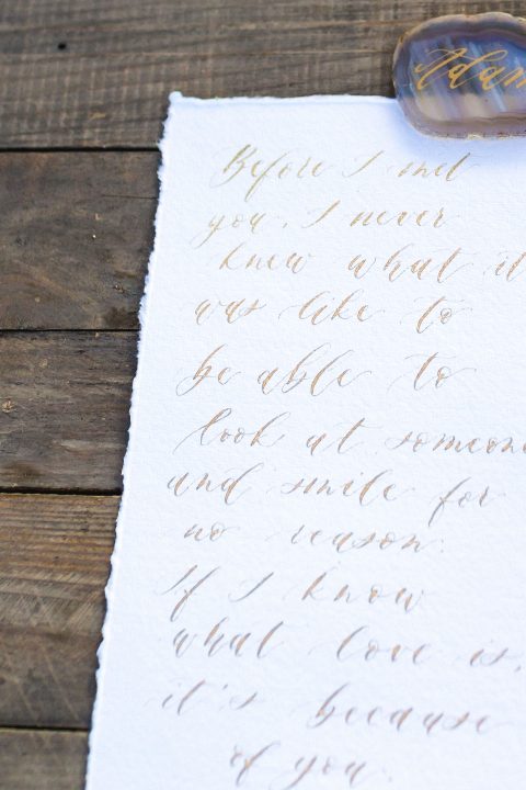Hochzeitswahn - Eine elegante handgeschriebene Notiz auf strukturiertem Papier neben einem zarten Glasstift, die den zeitlosen Charme der traditionellen Kalligraphie verkörpert.
