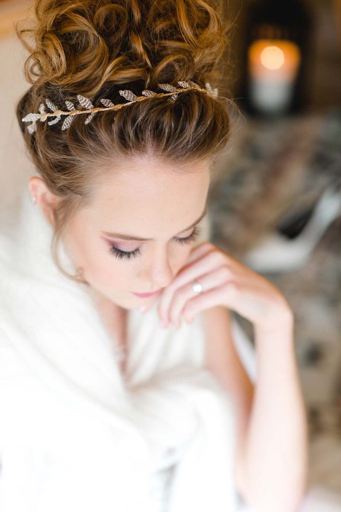 Hochzeitswahn - Eine Frau in einem weißen Gewand trägt eine aufwendige Hochsteckfrisur mit Schmetterlings-Haarschmuck, ihr Gesichtsausdruck ist nachdenklich und gelassen vor einem sanft verschwommenen Hintergrund.