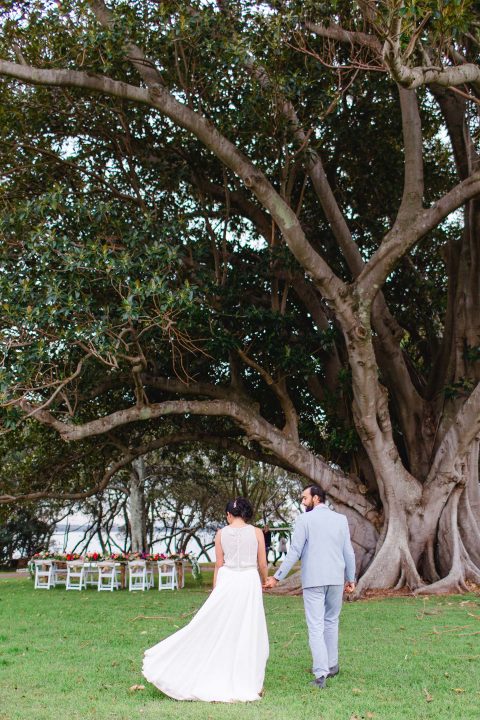Hochzeitswahn - Ein Paar geht Hand in Hand unter einem majestätischen Baum zu seiner Hochzeit, der Neuanfang und natürliche Gelassenheit symbolisiert.