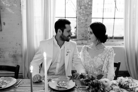 Hochzeitswahn - Ein frisch vermähltes Paar verbringt einen zärtlichen Moment an seinem Hochzeitstisch, umgeben von eleganter Dekoration, sanftem Kerzenlicht und einer Atmosphäre voller Romantik und Intimität.