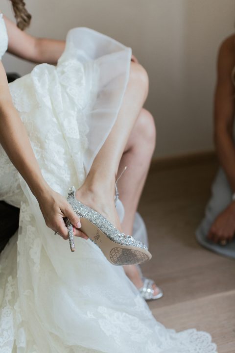 Hochzeitswahn - Eine Braut im Spitzenkleid schlüpft zart in einen glitzernden Stöckelschuh und präsentiert damit ein Hochzeitsritual voller Eleganz und Vorfreude.