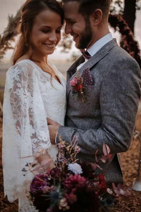 Hochzeitswahn - Braut und Bräutigam in Hochzeitskleidung teilen einen freudigen Moment im Freien in der Nähe der Heuchelberger Warte. Die Braut trägt ein Spitzenkleid und der Bräutigam einen grauen Anzug mit einem