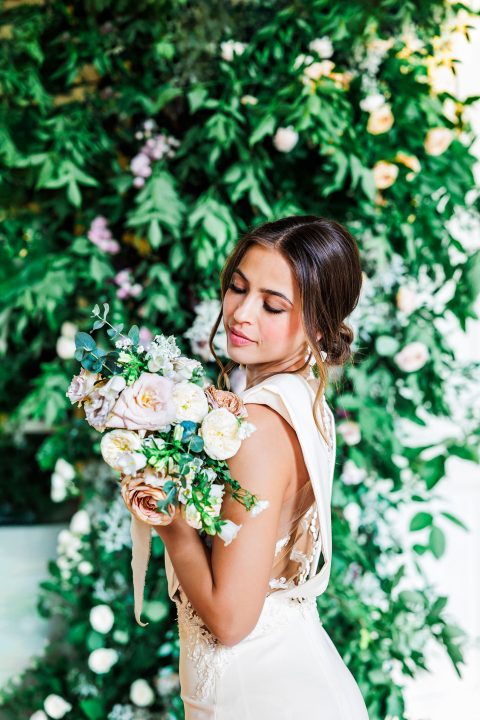 Hochzeitswahn - Eine Frau hält Blumen vor einer Blumenwand.