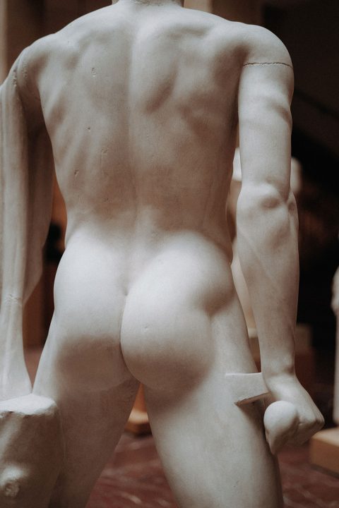 Hochzeitswahn - Eine Nahaufnahme der Rückseite einer klassischen weißen Marmorstatue, die komplizierte Details der menschlichen Muskulatur und Form hervorhebt.